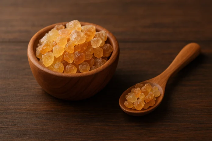 gum_arabic الصمغ العربي الهشاب داخل وعاء خشبي مع بعض الحبيبات حوله على ملعقة.