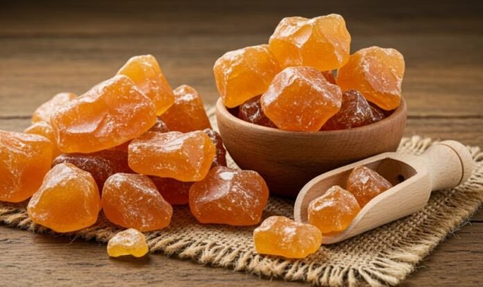 قطع من الصمغ العربي الطبيعي بلون ذهبي كهرماني، موضوعة في وعاء خشبي على طاولة، تظهر شكل الصمغ قبل طحنه واستخدامه