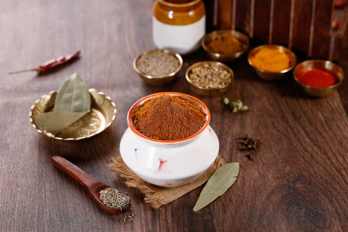 بهارات برياني اللحم في وعاء خزفي أبيض محاطة بتوابل هندية متنوعة على طاولة خشبية.